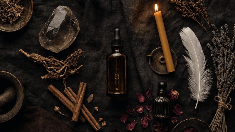 A curated elemental ritual toolkit laid out on dark linen: stones, botanicals, anointing oil, a small candle, dried flowers, and a smoke bundle representing all four elements