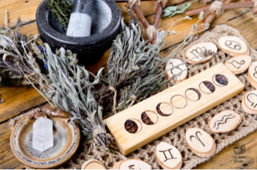 Wooden pentacle and wands on a wooden surface with herbs and stones.